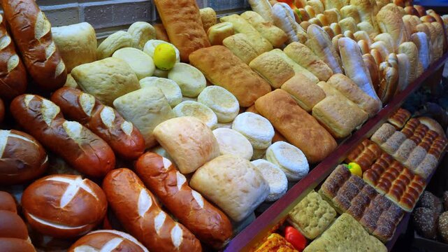 Brightly lit selection of traditional breads on a market display. A close up overhead perspective showcasing pretzel rolls, flatbreads, and a single yellow lemon among white buns.