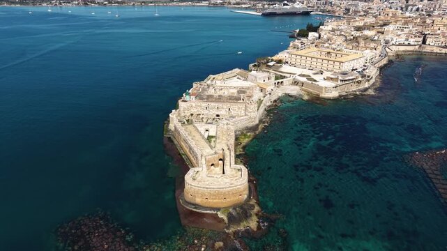 Aerial view of the historic Castello Maniace fortress on the tip of Ortygia island surrounded by the turquoise Mediterranean sea in Syracuse, Sicily, Italy.
