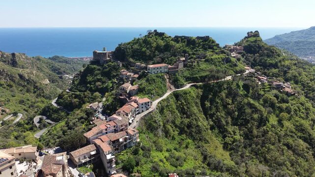 Aerial view of the historic hilltop village of Savoca with stone houses and winding roads overlooking the Mediterranean Sea in Savoca, Sicily, Italy.