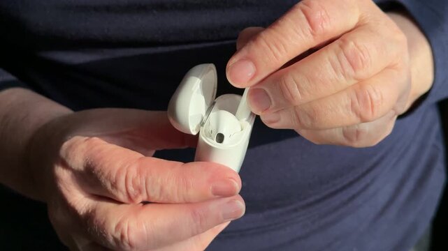 Closeup woman inserting earbud into case, gentle hand motion pressing earbud into slot of white charging case, visible click