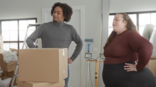 Man and plus size woman smile and hug by stacked moving boxes, man hand resting on box in building; affection moving together.