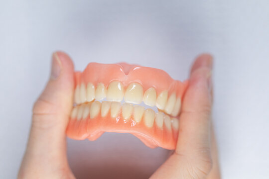 Used Full Denture Held Between Fingers, Dental Clinic Close-Up
