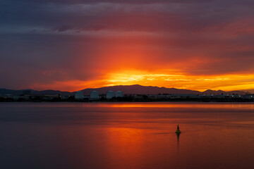 Fototapeta premium Fiery Sunset Over Industrial Waterfront with Calm Bay Water