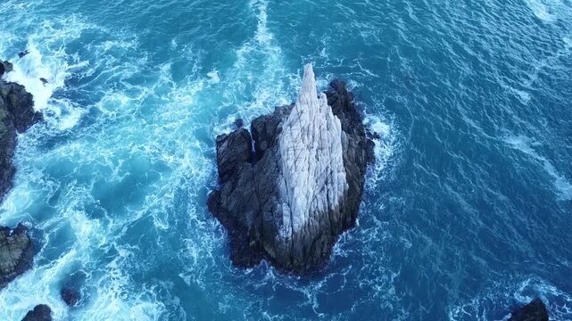 Drone aerial view frame of an isolated sharp white rocky pinnacle islet in a blue wavy ocean