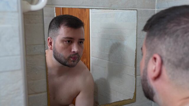 A young man rinsing shaving cream off his face with water in the bathroom in front of the mirror