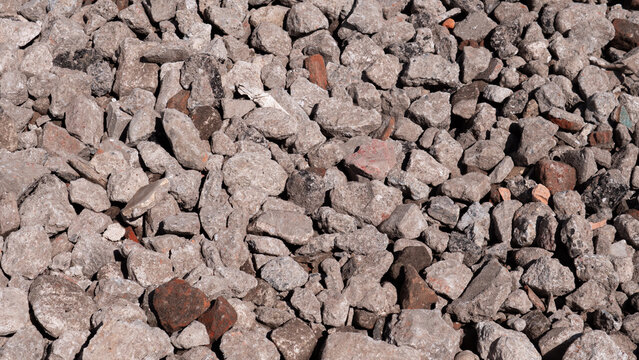 Close view of rough gray rocks and rubble scattered across the ground, creating a dense textured surface with natural earth tones and bright sunlight
