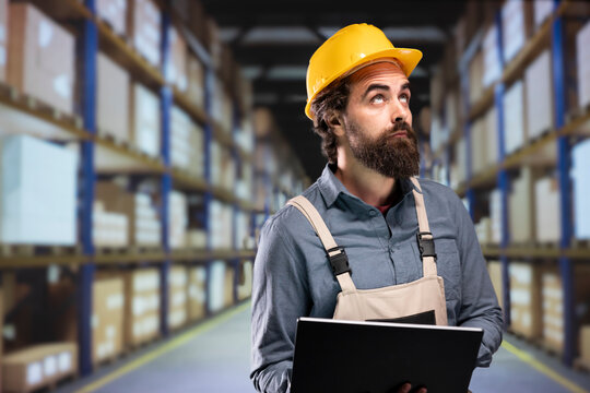 Storehouse worker verifying order list on laptop to provide cargo distribution, looking around warehouse to count all parcels ready for delivery. Industrial manager working on shipment logistics.