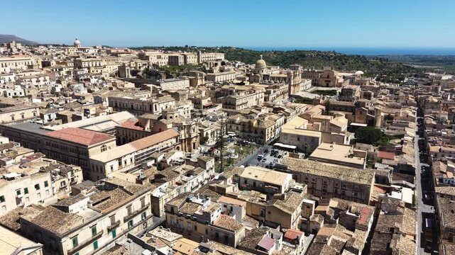 Aerial view of the historic Baroque architecture and limestone buildings of Noto with the Cathedral dome and the sea in the distance in Noto, Sicily, Italy.