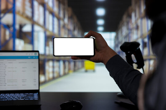 Industrial manager working on stock logistics with white screen, looking at mobile phone display with blank mockup layout. Employee in a depot handling orders and distribution with dispatch notes.