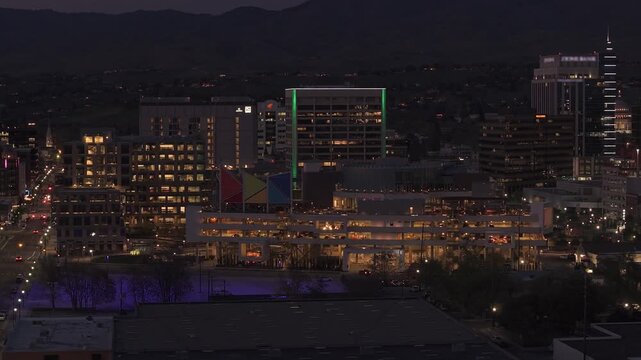 Nighttime slow panning drone shot of downtown Boise skyline viewed from the Boise River, Idaho. City lights glow brightly with traffic moving along 11th and 9th streets.