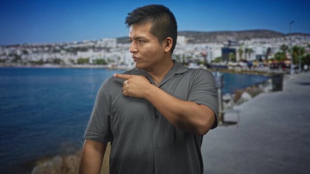 Man points finger to street on a seaside promenade, bare hand visible, turned profile and firm expression; confidence guidance.