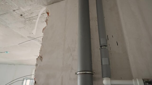 Close-up of industrial piping system with valve fittings on wall. Gray insulated pipes connected to white PVC pipe with black lever valve. Indoor utility setting with concrete wall background