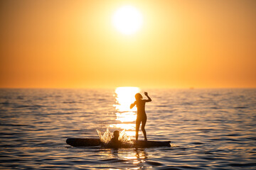 Fototapeta premium Friends playing on paddleboard at sunset in ocean