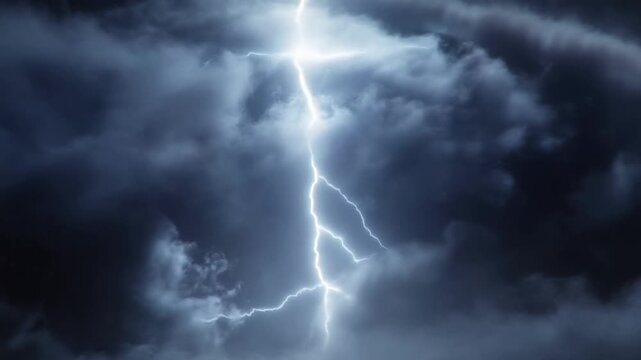 Slow motion static shot of lightning bolt striking and illuminating storm clouds in dark night sky over turbulent stormfront atmosphere