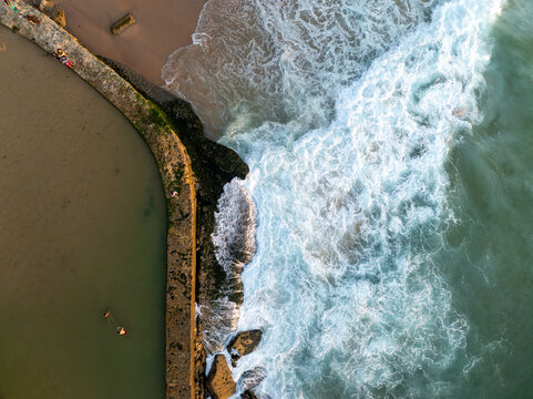 Aerial view of the natural swimming pool at Praia das Azenhas do Mar with ocean waves crashing against the stone wall in Colares, Lisbon, Portugal.