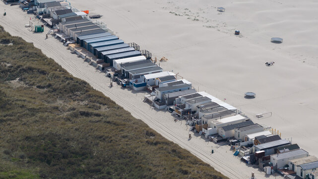 Aerial view of a long row of colorful beach huts situated between grassy dunes and a wide sandy shore Velsen-Noord, North Holland, Netherlands.