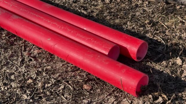 Red plastic pipes on soil, sunlit spring day, three pvc hot water tubes lying on gravel ready for replacement closeup view reveals