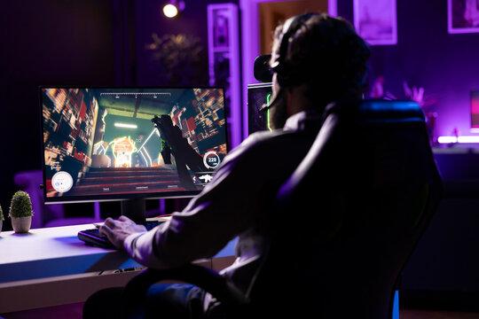 Player wearing headphones reaching final mission in FPS videogame, battling flying robots shooting laser bullets at him. Gamer playing game, fighting final boss, using headset to be immersed
