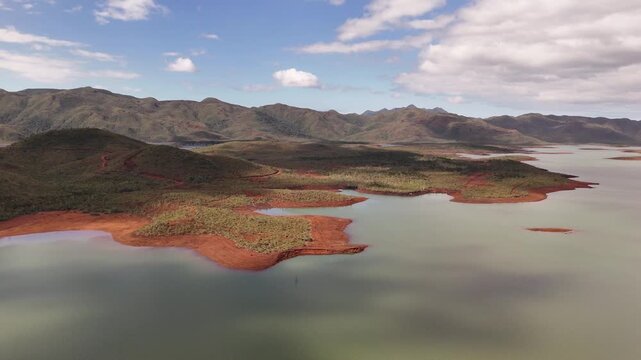 Aerial view of green lake with orange nickel shores, remote Blue River Provincial Park panorama with mountains and small vegetated islands, calm water under scattered clouds. Noumea, New Caledonia.