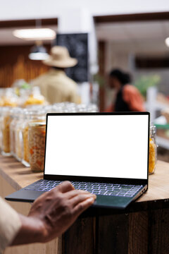 Detailed view of a digital laptop showing an isolated copyspace mockup template in an eco friendly supermarket. Close-up of african american person using minicomputer with blank white screen display.