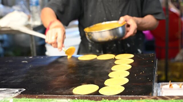 Thai street vendor preparing authentic local snacks at a bustling night market stall in Thailand; chef cooking delicious Asian street food with vibrant night lights and lively atmosphere.