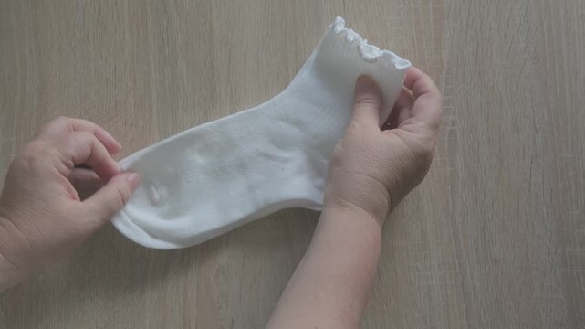Female hands check cotton socks for quality, meticulous inspection footwear, Elastic bands and fabric texture. Diabetic-friendly apparel. Clothing purchase