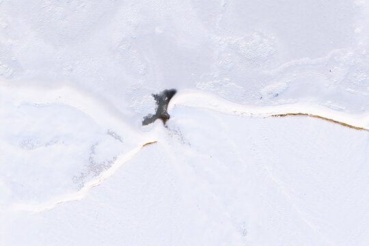 Aerial view of Zawadowskie Islands Nature Reserve featuring a frozen river landscape with thick snow and a small patch of open water, Masovian Voivodeship, Poland.