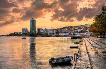 Obraz premium Golden hour sunset reflecting on the calm water of the bay with boats and the city skyline in Fort-de-France, Martinique, the Caribbean Lesser Antilles