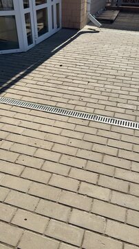 White pipe metal grate on pavement, patterned metal grate covers spillway installed across paving stones on footpath, sunlight