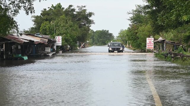 Trucks driving through a deeply flooded road during heavy monsoon season in Thailand, severe street flooding disaster