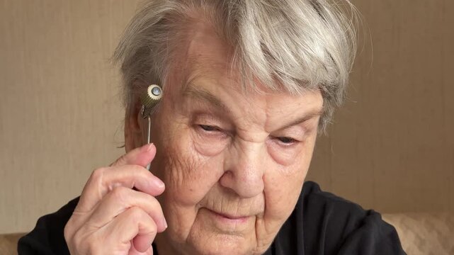 Elderly grandmother close-up massaging scalp with silver spiky roller scattering fine powder, wrinkled hands guiding metal tool