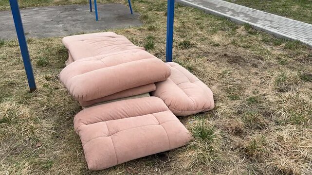 Courtyard pullup bar with sofa mats, spring day blue metal turnstile, stacked pink cushions from old sofa tossed on grass