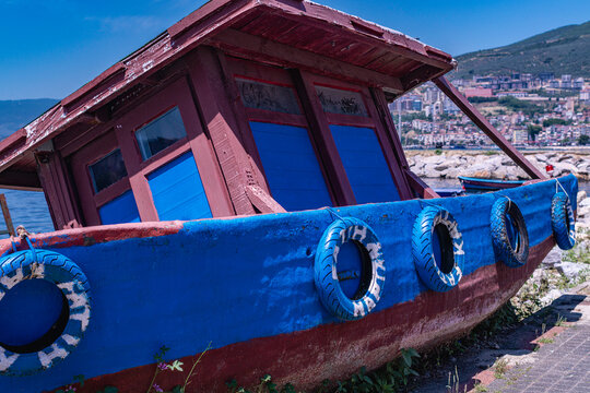 Close up of a vintage blue and red fishing boat with tire fenders parked near the harbor