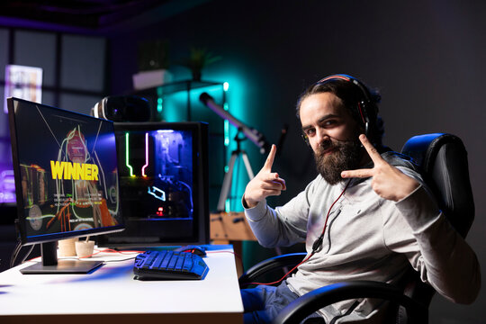 Jolly gamer in RGB lit home bragging after winning level in first person shooter, killing all enemies. Portrait of cheerful man celebrating, manifesting himself after being victorious in videogame