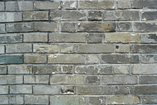 A close-up photograph of an aged, grey brick wall showcasing weathered textures, stains and worn mortar lines.