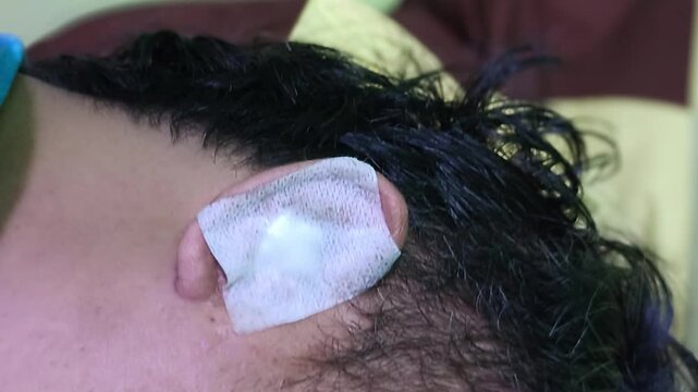 Close up of a man ear with white medical bandage plaster on it concept of ear injury wound healing after minor surgery skin infection treatment health care and first aid at home