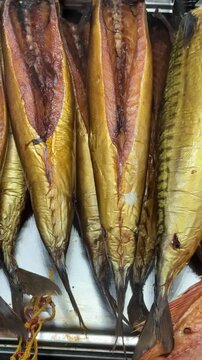 Cold smoked salmon balyk on counter, close-up of hanging golden fillets with visible salt crystals on metal rack inside fish shop