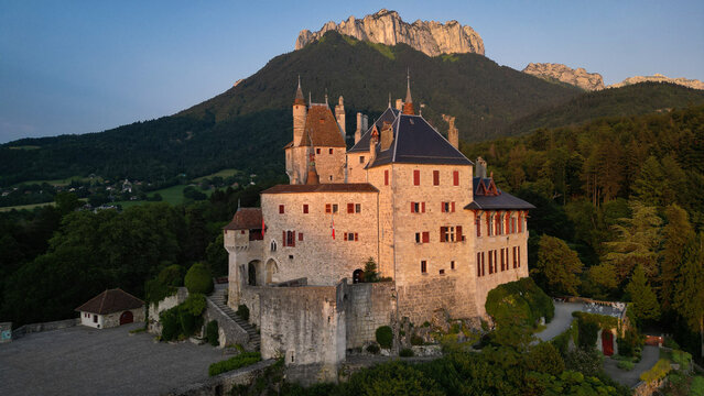 Menthon-Saint-Bernard, France - 09 July 2023: Aerial view of Chateau de Menthon-Saint-Bernard with its stone walls and turrets at sunset against the backdrop of the French Alps.