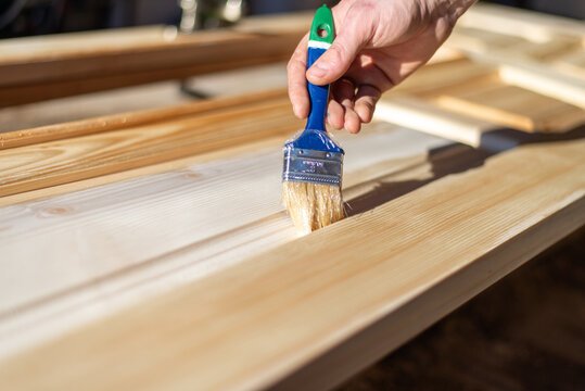 Close up of man hand applying clear varnish with brush on raw spruce wood door