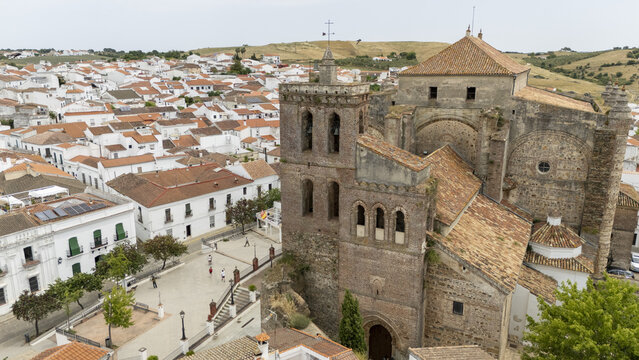 Cazalla de la Sierra, Spain - 31 May 2026: Aerial view of the Iglesia de Nuestra Senora de la Consolacion with its massive stone bell tower overlooking a town square and white houses.