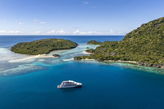 Nadi, Fiji - 05 May 2026: Aerial view of a white cruise ship anchored in the turquoise waters of the Yasawa Islands with lush green hills and coral reefs under a clear blue sky.