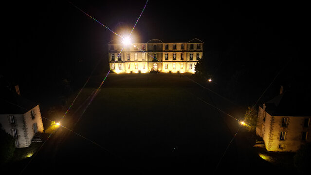 Loyat, France - 01 September 2023: Aerial view of Chateau de Loyat illuminated at night with a bright starburst light effect and dark surrounding grounds.