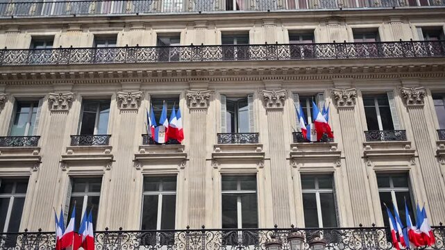 Classic parisian building architecture featuring french flags during national celebration.