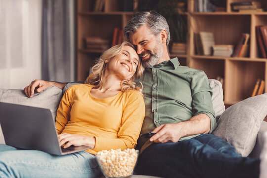 Happy Senior, Caucasian Man And Woman, Enjoying Movie Night Together At Home, Sitting Comfortably On Couch With Laptop And Popcorn, Smiling And Relaxed. Family Concept