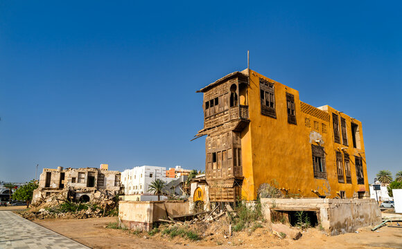 A bright yellow ruined building with traditional wooden latticed windows and balconies in the Yanbu Historic Area of Saudi Arabia.