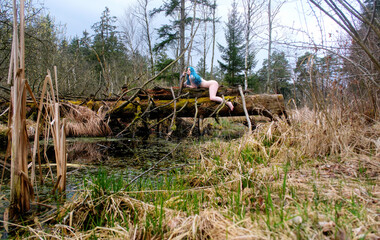 Sexy nude woman with turquoise hair lies atop a mossy fallen tree in a swampy forest, merging with nature in a raw, primal, and surreal scene of wild harmony and contrast © ullision