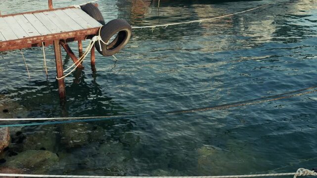 Wooden Pier With Rubber Tires And Mooring Ropes At Harbor