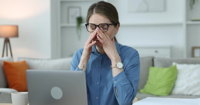 Workaholic. Overwhelmed woman in glasses at wooden desk with laptop and stack of documents indoors. Camera moving forward