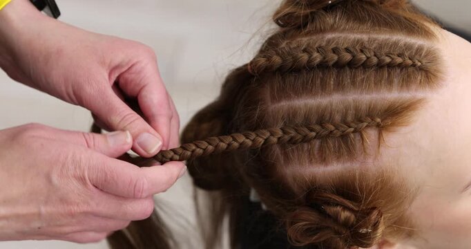 Hairstylist braiding teenage girl's hair in salon, closeup. Camera moving up and down
