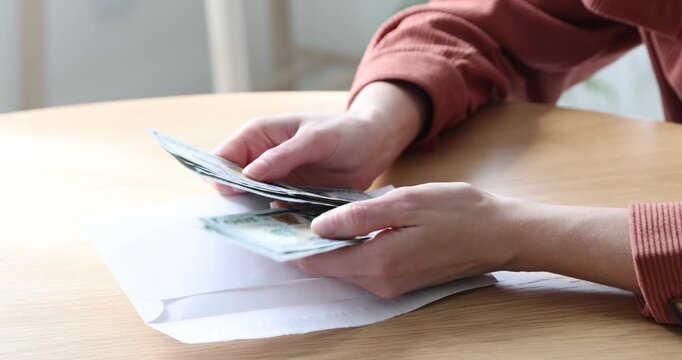 Woman opening envelope with dollar banknotes indoors, closeup